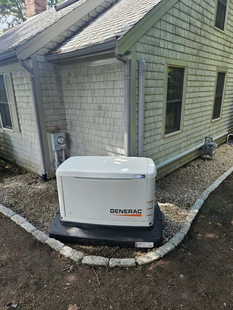 Generac standby generator installed on a paver pad beside a shingle-sided home